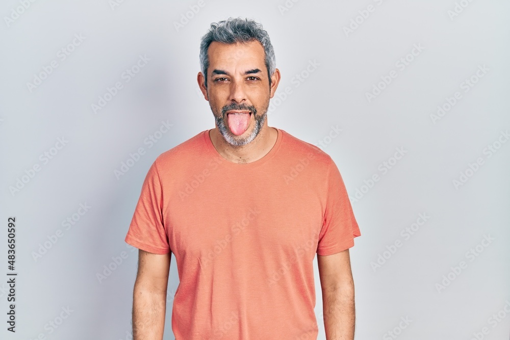 Handsome middle age man with grey hair wearing casual t shirt sticking tongue out happy with funny expression. emotion concept.