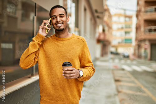 Young african american man talking on the smartphone drinking coffee at the city.