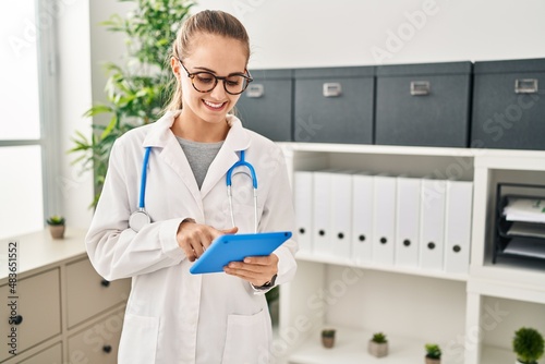 Young blonde woman wearing doctor uniform using touchpad working at clinic