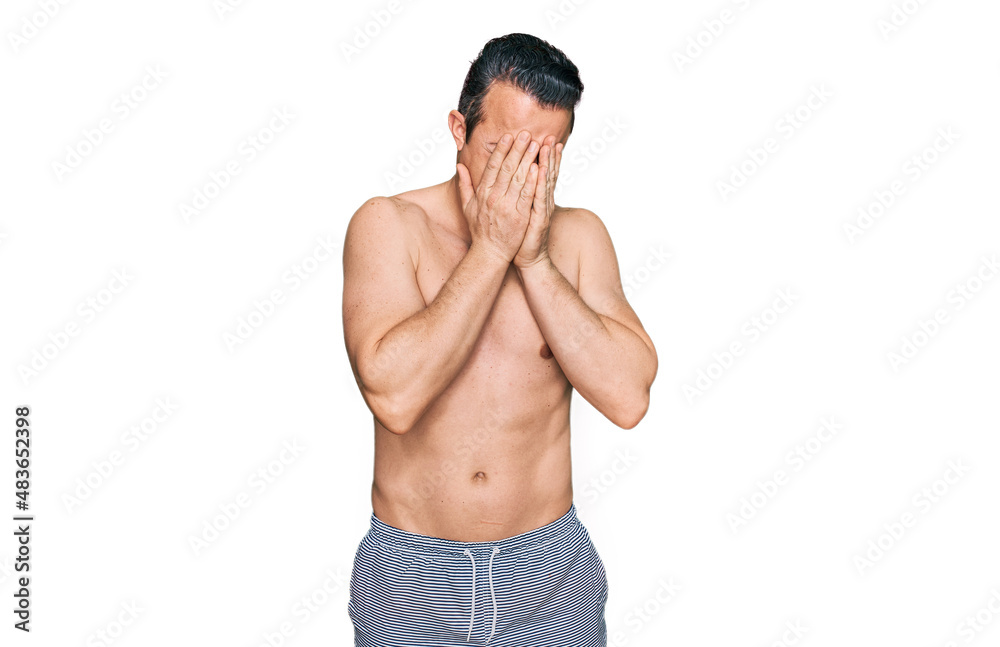 Fototapeta premium Handsome young man wearing swimwear shirtless with sad expression covering face with hands while crying. depression concept.