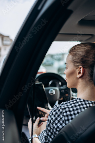 Beautiful young woman working as used car seller. She is using digital tablet and checking car condition before customer or buyer. Used vehicle dealership. © Dusko