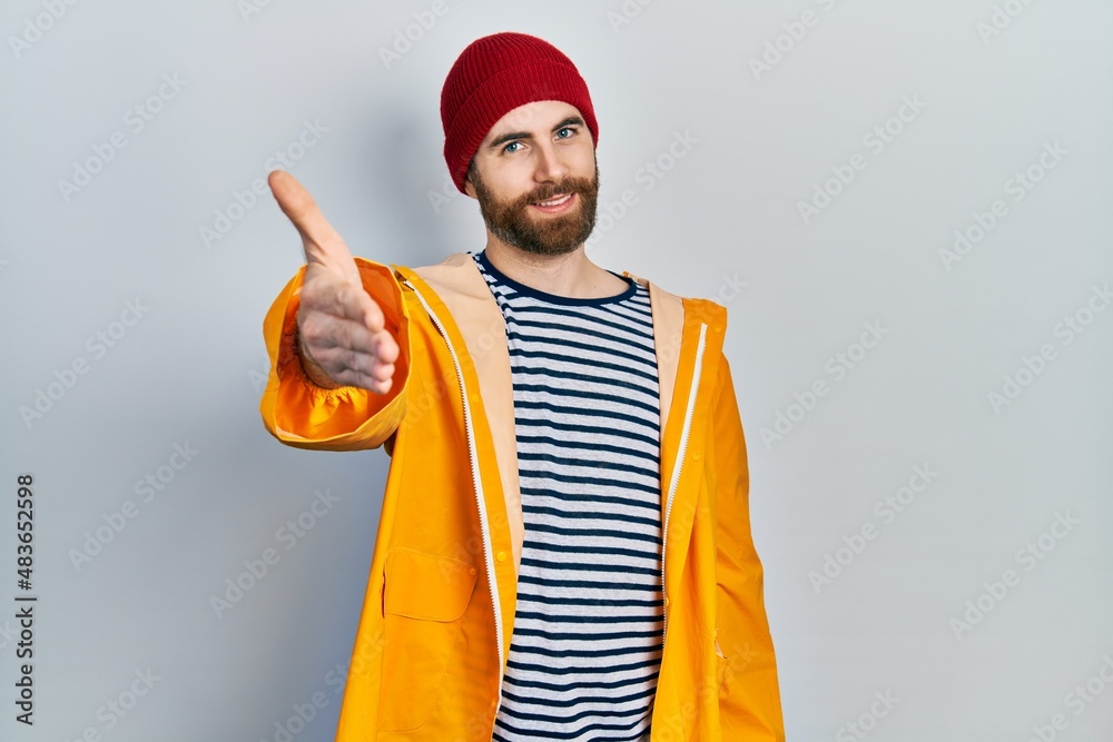 Caucasian man with beard wearing yellow raincoat smiling cheerful offering palm hand giving assistance and acceptance. Caucasian man with beard wearing yellow raincoat smiling cheerful offering palm hand giving assistance and acceptance.