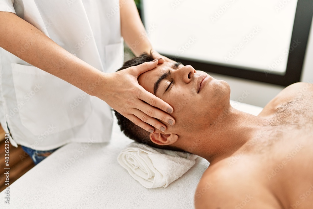 Obraz premium Young hispanic man relaxed having facial massage at beauty center