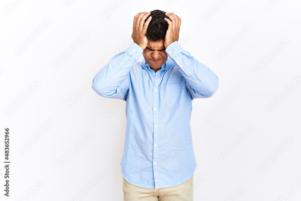 Young hispanic man wearing business shirt standing over isolated background suffering from headache desperate and stressed because pain and migraine. hands on head. Young hispanic man wearing business shirt standing over isolated background suffering from headache desperate and stressed because pain and migraine. hands on head.
