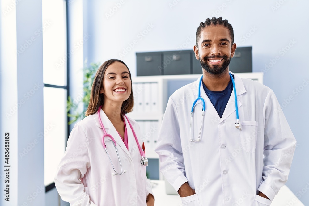 Man and woman wearing doctor uniform smiling confident standing at clinic Man and woman wearing doctor uniform smiling confident standing at clinic