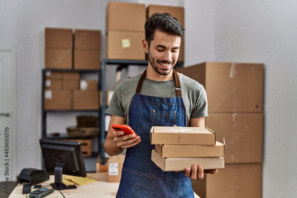 © Krakenimages.com - Young hispanic man business worker using smartphone holding packages at storehouse © Krakenimages.com - Young hispanic man business worker using smartphone holding packages at storehouse