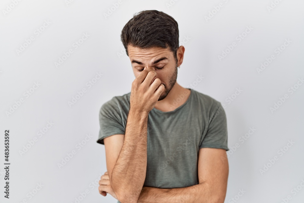 Young hispanic man with beard wearing casual t shirt over white background tired rubbing nose and eyes feeling fatigue and headache. stress and frustration concept. Young hispanic man with beard wearing casual t shirt over white background tired rubbing nose and eyes feeling fatigue and headache. stress and frustration concept.