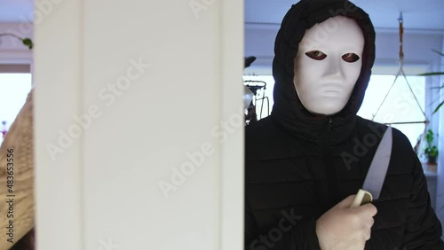 Young Caucasian Woman Coming Home Underssing Unaware of Maniac Serial Killer Wearing Creepy Face Mask Hiding Lurking in Next Room photo