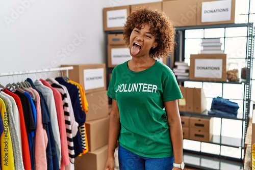 Young african american woman wearing volunteer t shirt at donations stand sticking tongue out happy with funny expression. emotion concept.