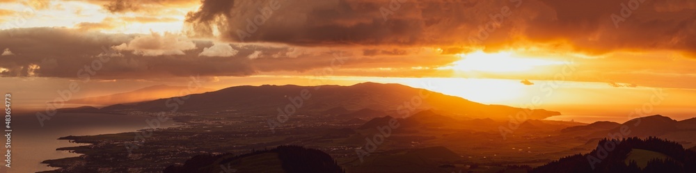 Sunrise over landscape with mountains, orange light, sun rising.