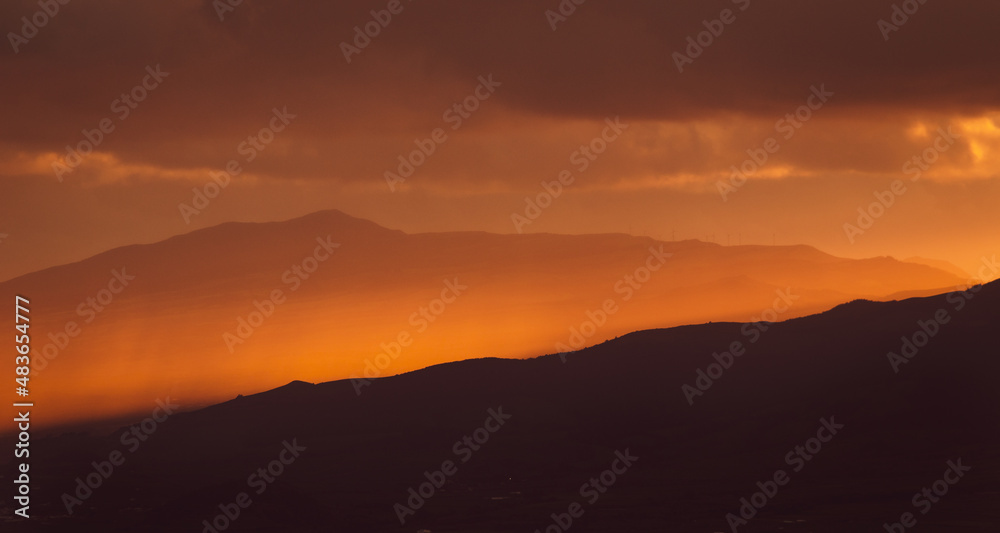 Sunrise over landscape with mountains, orange light, sun rising.