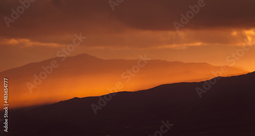 Sunrise over landscape with mountains, orange light, sun rising.