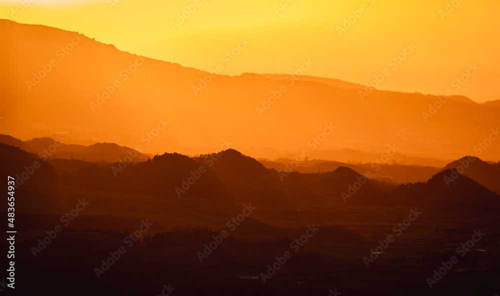 Sunrise over landscape with mountains, orange light, sun rising.