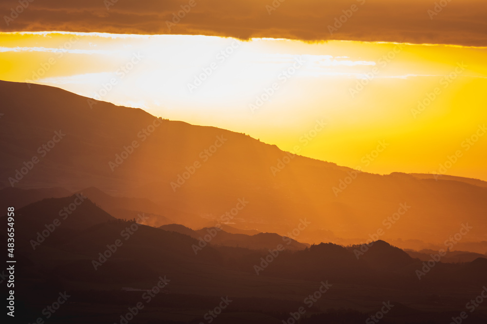 Sunrise over landscape with mountains, orange light, sun rising.