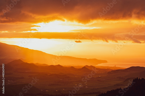 Sunrise over landscape with mountains, orange light, sun rising. © Ayla Harbich