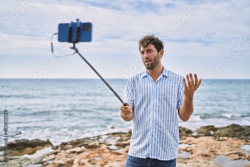 Young hispanic man smiling happy having video call using smartphone at the beach.