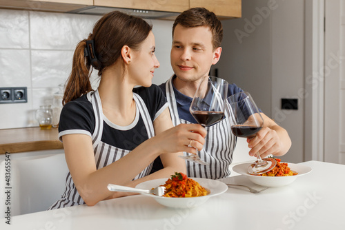 Valentine day romantic dinner at home. Happy couple smiling, clinking glasses and eating pasta with wine at kitchen. Concept of domestic lifestyle, love, happy marriage and togetherness.