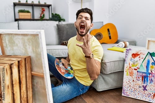 Fotótapéta Young man with beard painting canvas at home crazy and mad shouting and yelling with aggressive expression and arms raised