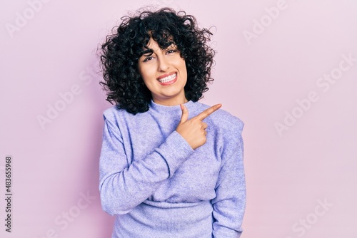Young middle east woman wearing casual clothes cheerful with a smile of face pointing with hand and finger up to the side with happy and natural expression on face