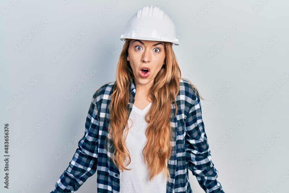 Young caucasian woman wearing architect hardhat scared and amazed with open mouth for surprise, disbelief face Young caucasian woman wearing architect hardhat scared and amazed with open mouth for surprise, disbelief face