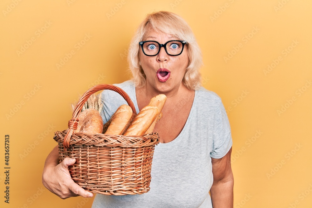 Middle age blonde woman holding wicker basket with bread scared and amazed with open mouth for surprise, disbelief face Middle age blonde woman holding wicker basket with bread scared and amazed with open mouth for surprise, disbelief face