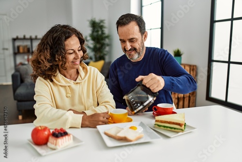 Middle age hispanic couple smiling happy sitting on the table having breakfast at home.