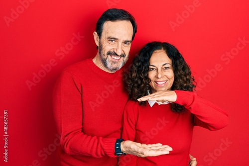 Middle age couple of hispanic woman and man hugging and standing together gesturing with hands showing big and large size sign, measure symbol. smiling looking at the camera. measuring concept. © Krakenimages.com