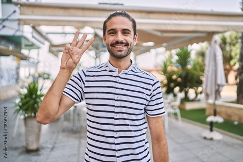 Young hispanic man with beard outdoors at the city showing and pointing up with fingers number three while smiling confident and happy. © Krakenimages.com