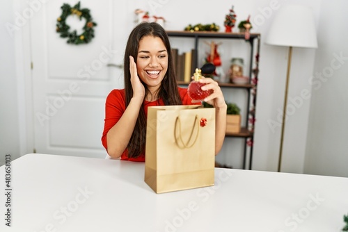 Young latin woman holding perfume of gift bag sitting by christmas decor at home © Krakenimages.com