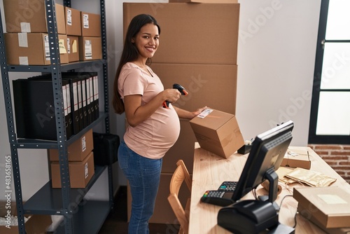Fototapeta Naklejka Na Ścianę i Meble -  Young latin woman pregnant business worker scanning package label at office