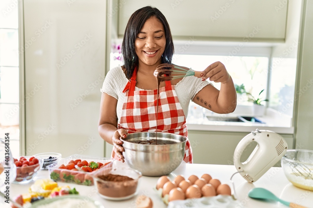 Hispanic brunette woman preparing chocolate cake with whisk at the kitchen Hispanic brunette woman preparing chocolate cake with whisk at the kitchen