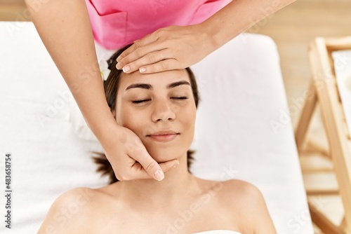 Young hispanic woman smiling confident having facial massage at beauty center.