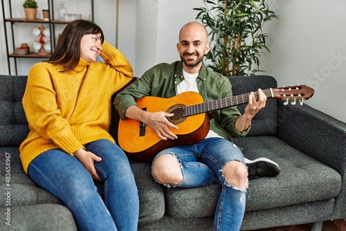 Young hispanic couple smiling happy playing classical guitar sitting on the sofa at home.