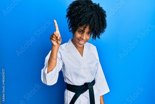 African american woman with afro hair wearing karate kimono and black belt showing and pointing up with finger number one while smiling confident and happy.