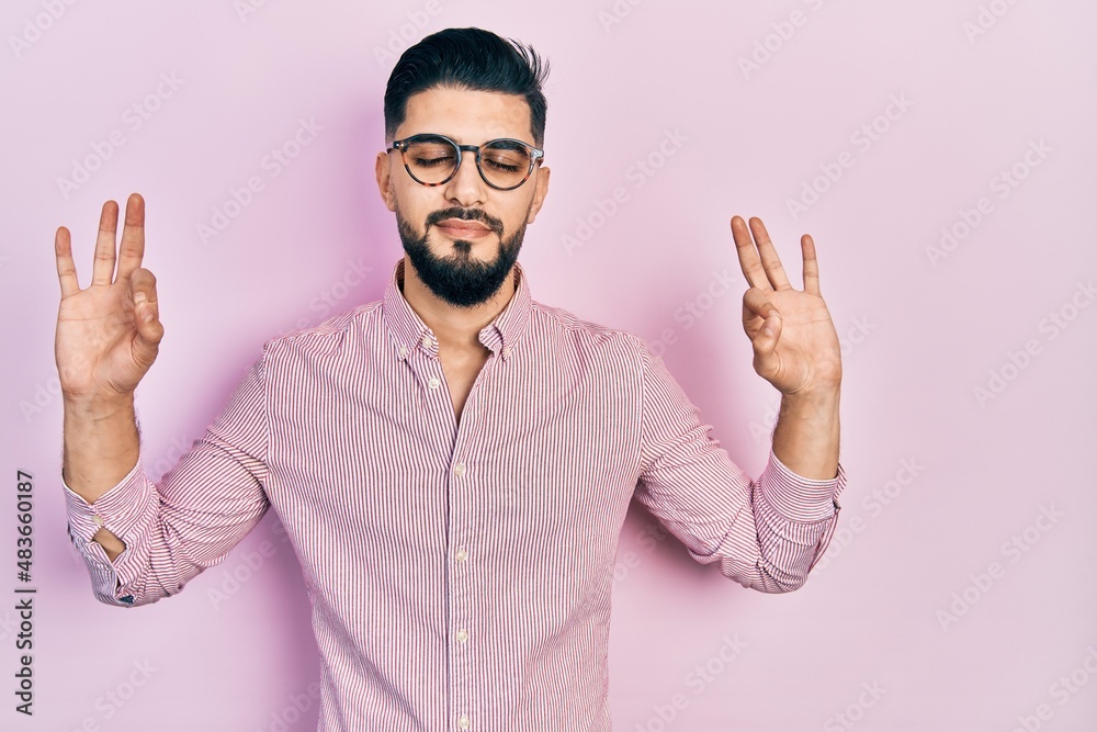 Handsome man with beard wearing casual shirt and glasses relax and smiling with eyes closed doing meditation gesture with fingers. yoga concept. Handsome man with beard wearing casual shirt and glasses relax and smiling with eyes closed doing meditation gesture with fingers. yoga concept.