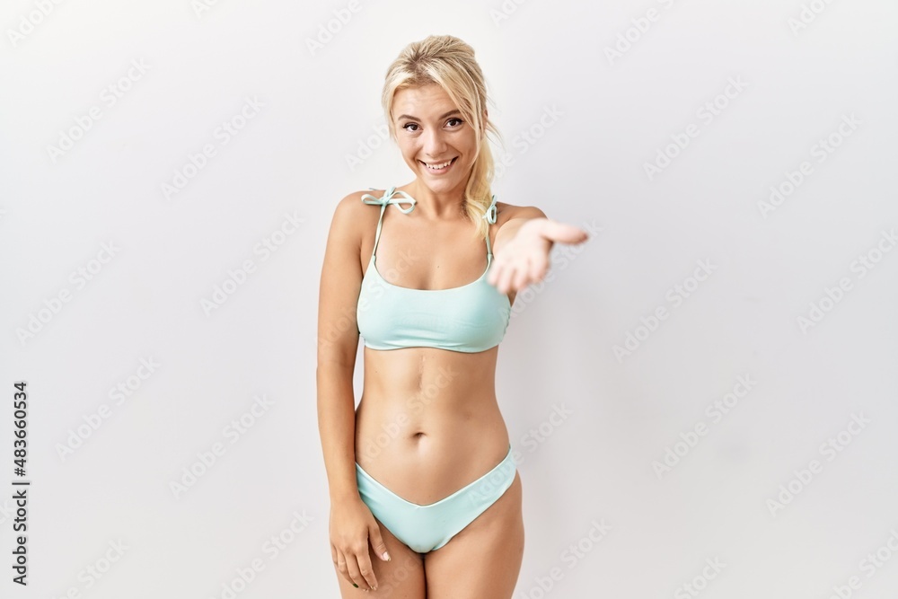 Young caucasian woman wearing bikini over isolated background smiling friendly offering handshake as greeting and welcoming. successful business. Young caucasian woman wearing bikini over isolated background smiling friendly offering handshake as greeting and welcoming. successful business.