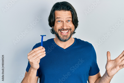 Middle age caucasian man holding razor celebrating achievement with happy smile and winner expression with raised hand