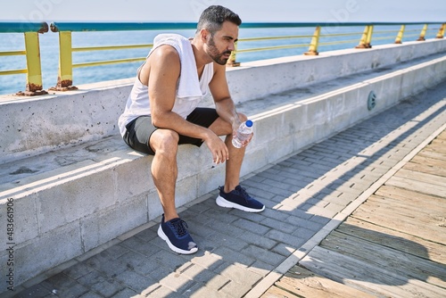 Hispanic man resting sitting on a bench after working out outdoors on a sunny day