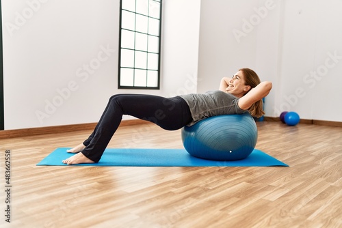 Middle age caucasian woman smiling confident training using fit ball at sport center