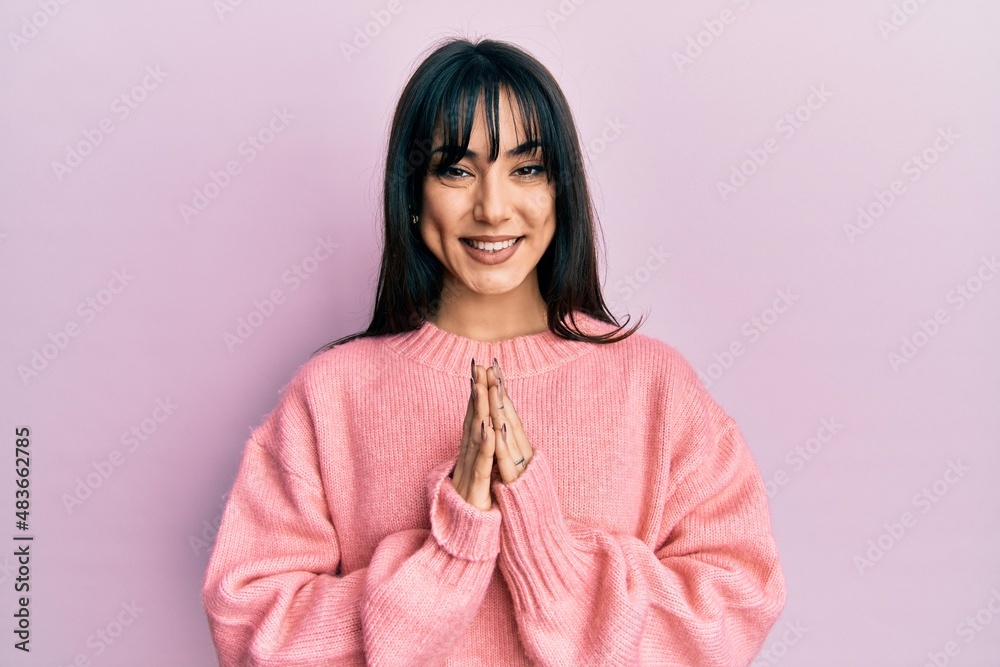 Fototapeta premium Young brunette woman with bangs wearing casual winter sweater praying with hands together asking for forgiveness smiling confident.