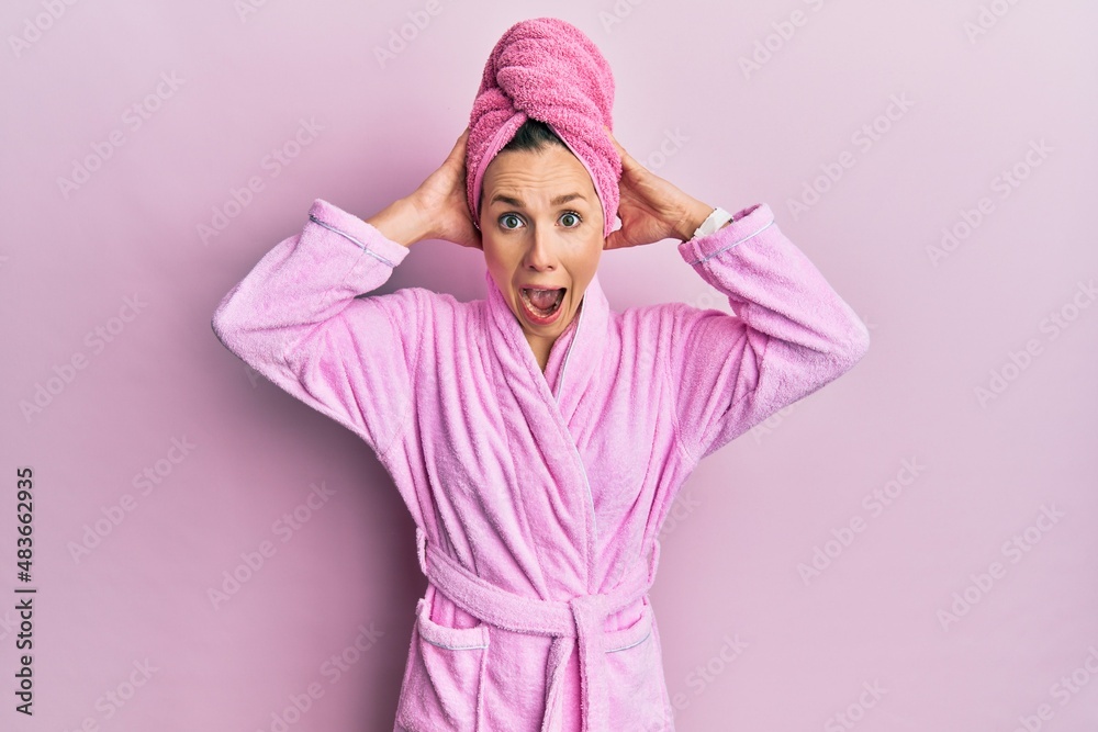 Young blonde woman wearing shower towel cap and bathrobe crazy and scared with hands on head, afraid and surprised of shock with open mouth Young blonde woman wearing shower towel cap and bathrobe crazy and scared with hands on head, afraid and surprised of shock with open mouth