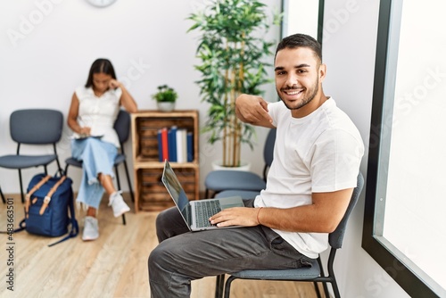 Young people sitting at waiting room working with laptop pointing finger to one self smiling happy and proud