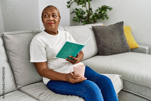 Senior african american woman drinking coffee reading book at home