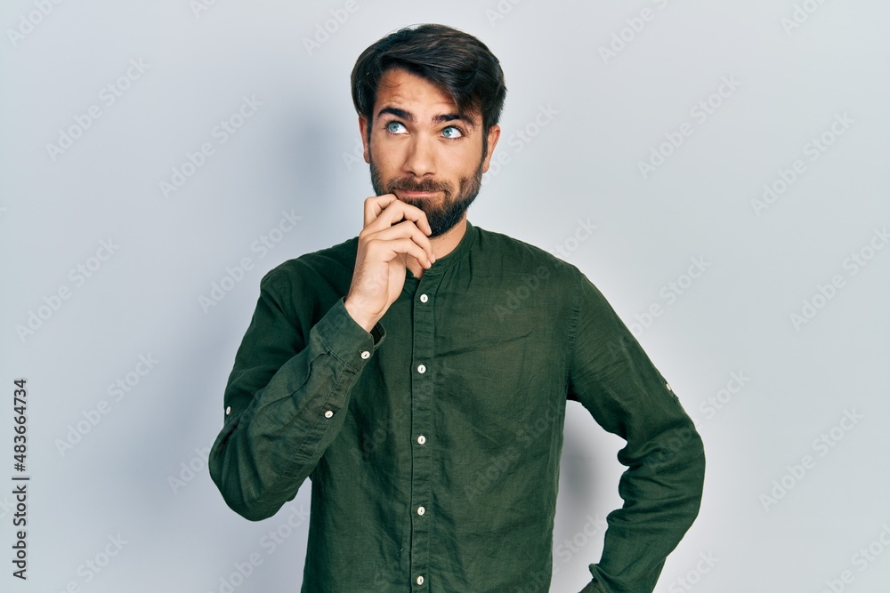 Young hispanic man wearing casual clothes thinking concentrated about doubt with finger on chin and looking up wondering Young hispanic man wearing casual clothes thinking concentrated about doubt with finger on chin and looking up wondering