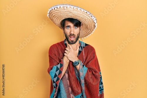 Young hispanic man holding mexican hat shouting and suffocate because painful strangle. health problem. asphyxiate and suicide concept.