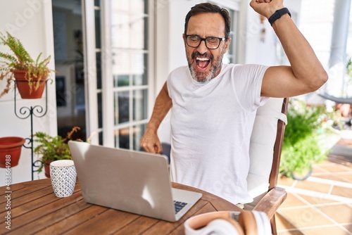 Middle age man using computer laptop at home dancing happy and cheerful, smiling moving casual and confident listening to music