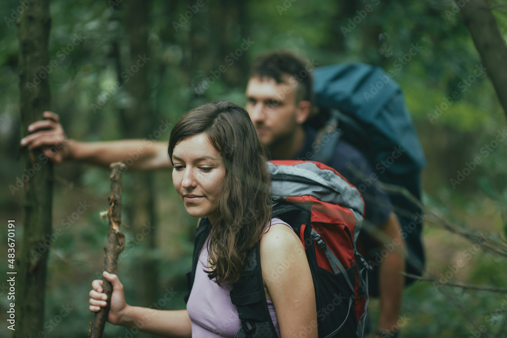 Two friends moving through a forest on a hiking vacation, using walking stick branches, guiding their way through the woods