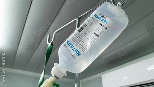 A bottle of NaCI sodium chloride fluid setup for a patient's IV intravenous hydration drip, close up in hospital ward photo