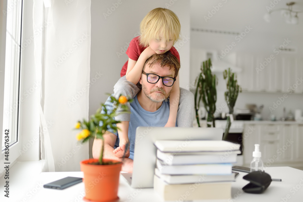 Man is working from home with laptop during quarantine. Home office and parenthood at same time. Exhausted parent with hyperactive child. Man is working from home with laptop during quarantine. Home office and parenthood at same time. Exhausted parent with hyperactive child.