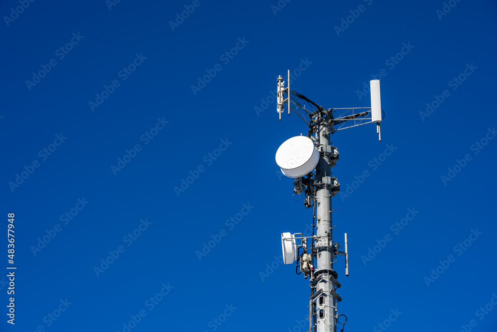 Closeup of wireless cell site antennas on a monopole tower against a clear blue sky
